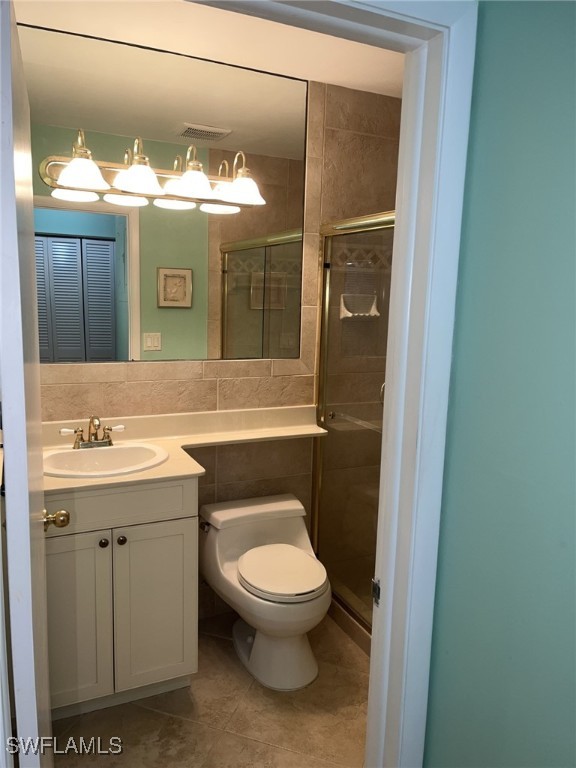 full bath with visible vents, toilet, vanity, a stall shower, and tile walls