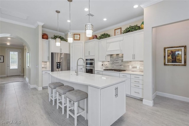 2720 Amaranda Ct, Naples, FL 34114 - kitchen with stainless steel appliances, custom range hood, an island with sink, white cabinets, and decorative light fixtures