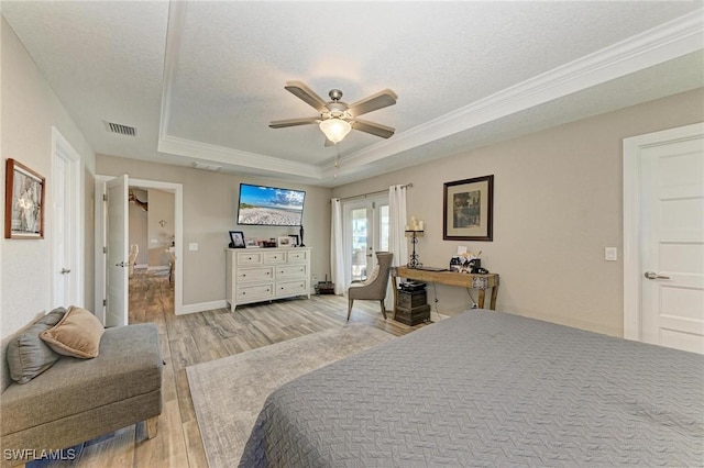 bedroom with a tray ceiling, light hardwood / wood-style floors, french doors, and a textured ceiling