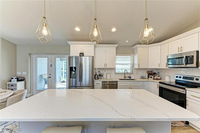 kitchen featuring pendant lighting, sink, stainless steel appliances, white cabinets, and a kitchen bar