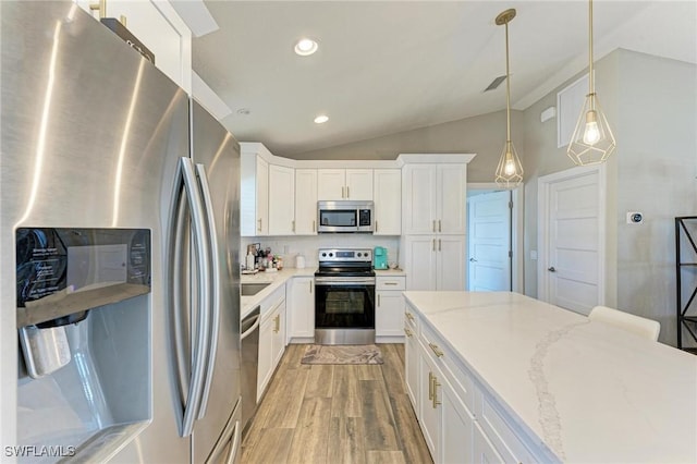 kitchen with appliances with stainless steel finishes, white cabinetry, light stone countertops, decorative light fixtures, and vaulted ceiling