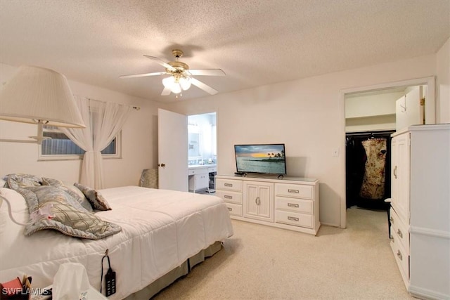 bedroom featuring a walk in closet, light carpet, a closet, a textured ceiling, and a ceiling fan