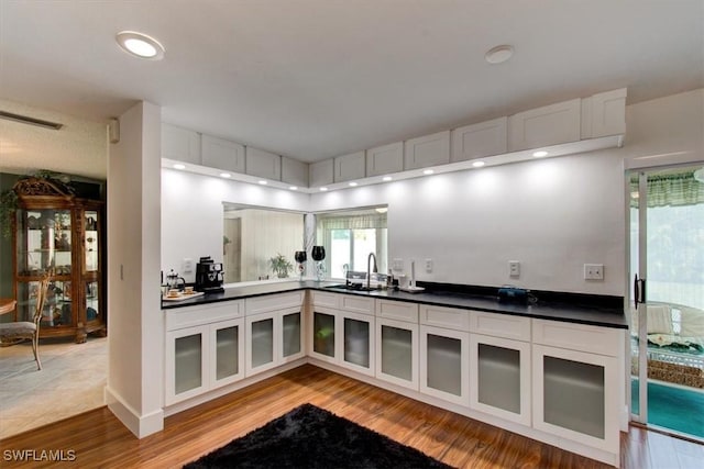 kitchen featuring a sink, dark countertops, wood finished floors, white cabinetry, and glass insert cabinets