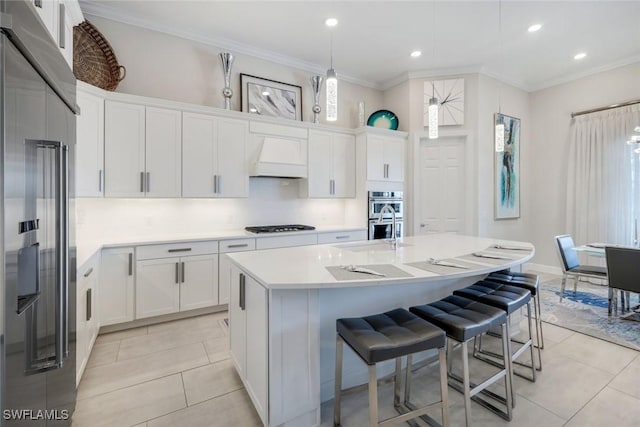 kitchen with white cabinetry, an island with sink, stainless steel appliances, custom range hood, and crown molding