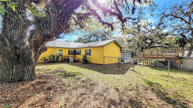 back of property featuring a wooden deck, cooling unit, and a lawn