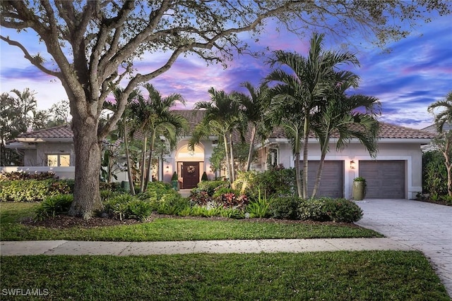 view of front of property featuring decorative driveway, an attached garage, a tile roof, and stucco siding