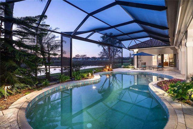 pool at dusk featuring a water view, a patio area, and a lanai