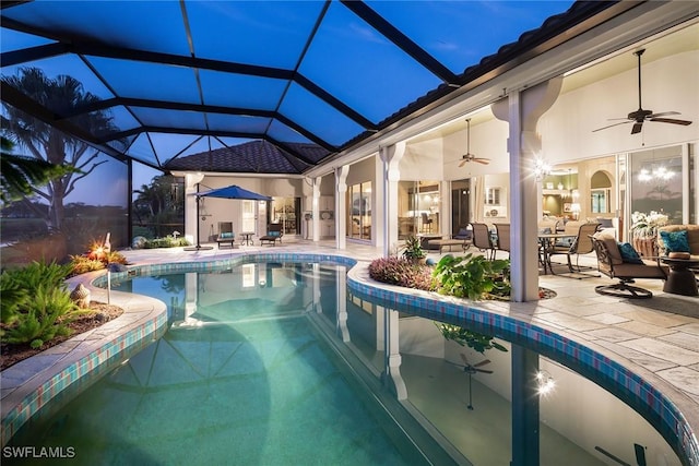 pool at dusk with ceiling fan, a patio, and glass enclosure