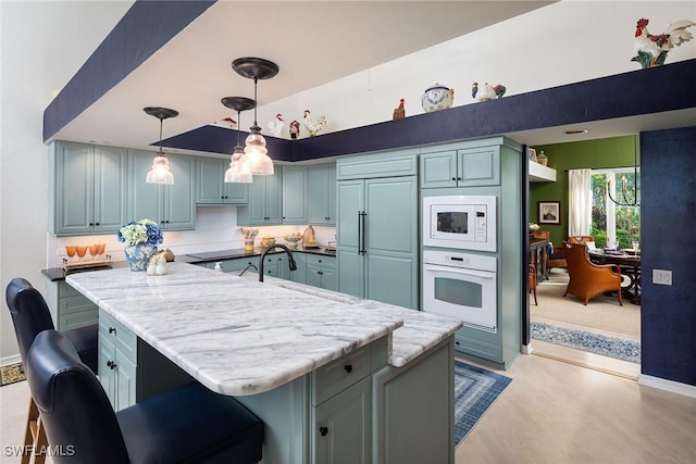 kitchen featuring sink, a breakfast bar area, built in appliances, hanging light fixtures, and decorative backsplash