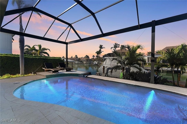 pool at dusk featuring a water view, a patio, and glass enclosure