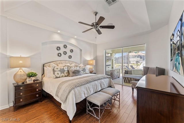 bedroom with ceiling fan, a tray ceiling, access to outside, and wood-type flooring