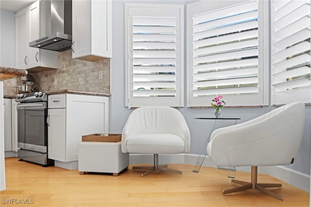 interior space featuring light hardwood / wood-style flooring, wall chimney exhaust hood, white cabinetry, and stainless steel range