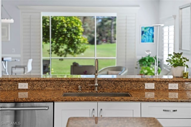 kitchen with sink, stainless steel dishwasher, dark stone counters, and white cabinetry