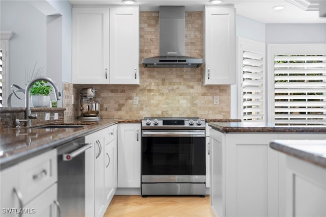 kitchen with dark stone countertops, backsplash, white cabinetry, wall chimney range hood, and stainless steel appliances