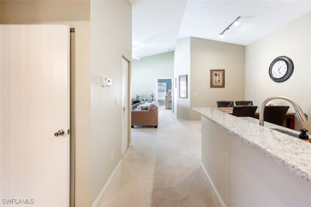 hall with track lighting, baseboards, lofted ceiling, a sink, and light colored carpet