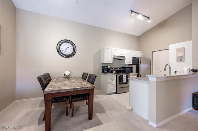 kitchen with a peninsula, light stone countertops, stainless steel appliances, under cabinet range hood, and white cabinetry