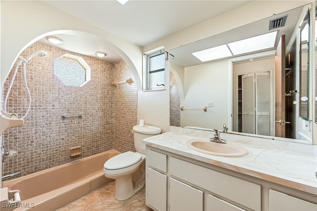 full bathroom featuring tiled shower / bath, a skylight, tile patterned flooring, vanity, and toilet