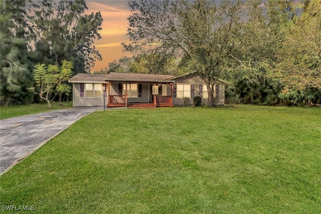 ranch-style home featuring driveway, a porch, and a lawn