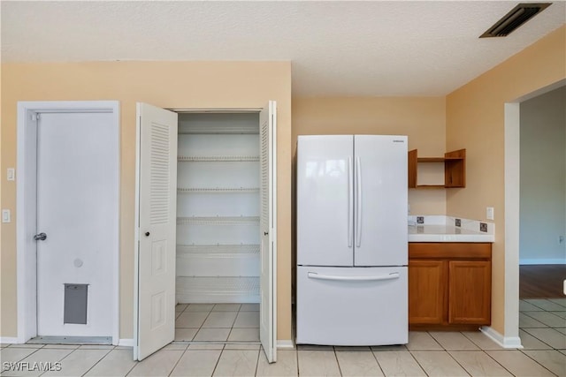 4001 E Sunflower Cir, Labelle, FL 33935 - kitchen with light countertops, visible vents, brown cabinets, light tile patterned floors, and freestanding refrigerator