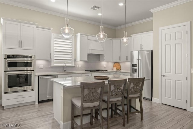 kitchen with appliances with stainless steel finishes, hanging light fixtures, a center island, white cabinets, and a kitchen bar