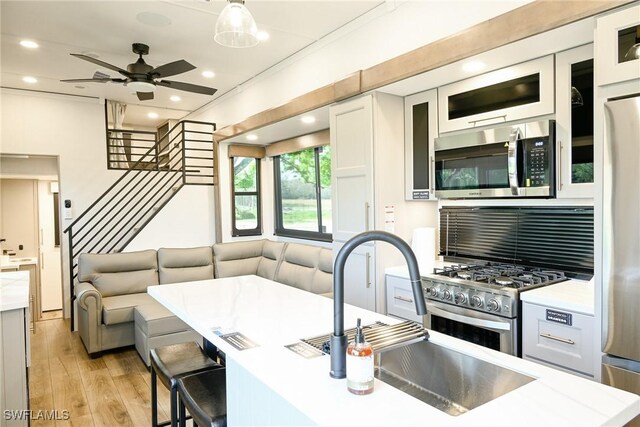 kitchen featuring appliances with stainless steel finishes, a breakfast bar, decorative light fixtures, white cabinetry, and light wood-type flooring