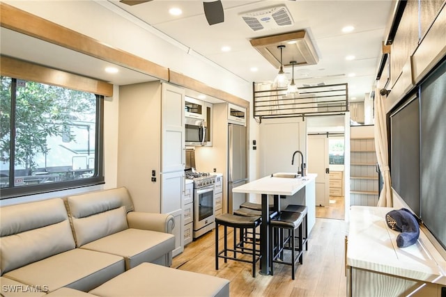 kitchen with white cabinetry, hanging light fixtures, appliances with stainless steel finishes, a kitchen breakfast bar, and light hardwood / wood-style floors