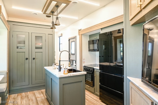 kitchen featuring gray cabinets, pendant lighting, an island with sink, black appliances, and light wood-type flooring