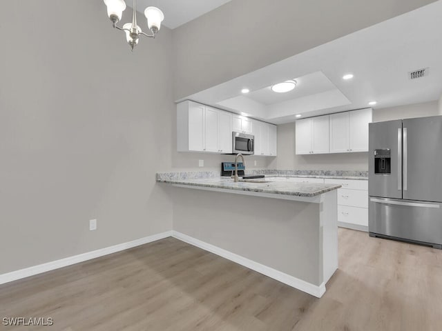 kitchen featuring a sink, baseboards, appliances with stainless steel finishes, light wood-type flooring, and a tray ceiling