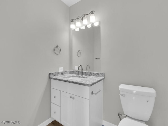 half bathroom featuring vanity, toilet, and baseboards