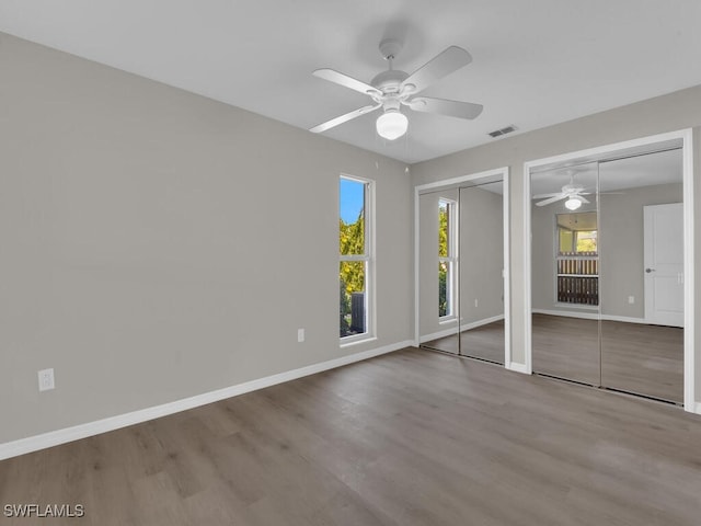 unfurnished bedroom featuring baseboards, wood finished floors, visible vents, and multiple closets