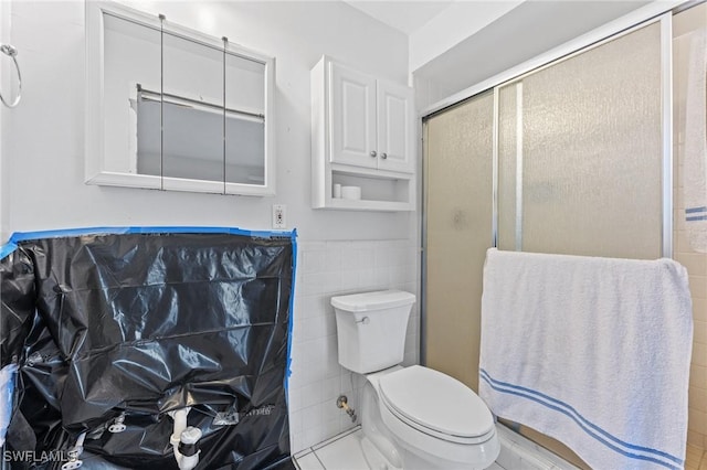 bathroom featuring toilet, an enclosed shower, and tile walls