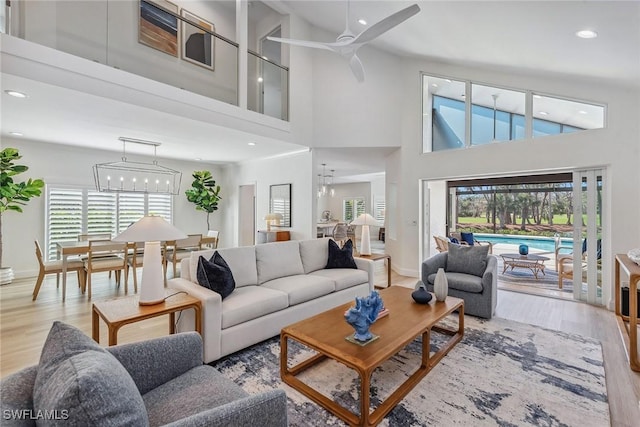 living room with a towering ceiling, ceiling fan with notable chandelier, and light hardwood / wood-style flooring