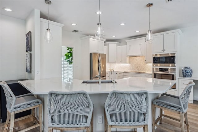 kitchen with a breakfast bar area, appliances with stainless steel finishes, decorative backsplash, white cabinets, and decorative light fixtures