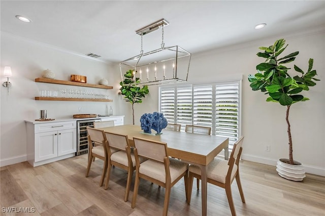 dining room featuring indoor bar, ornamental molding, and light hardwood / wood-style floors