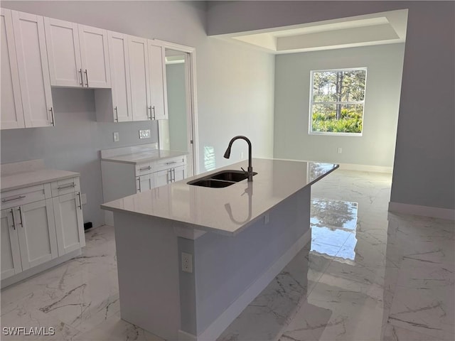 kitchen with light stone countertops, a kitchen island with sink, sink, and white cabinets