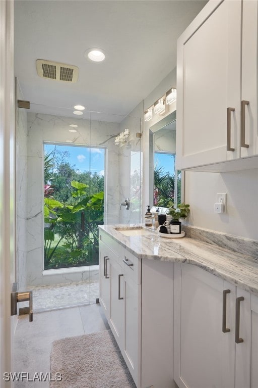 bathroom with visible vents, plenty of natural light, vanity, and a marble finish shower