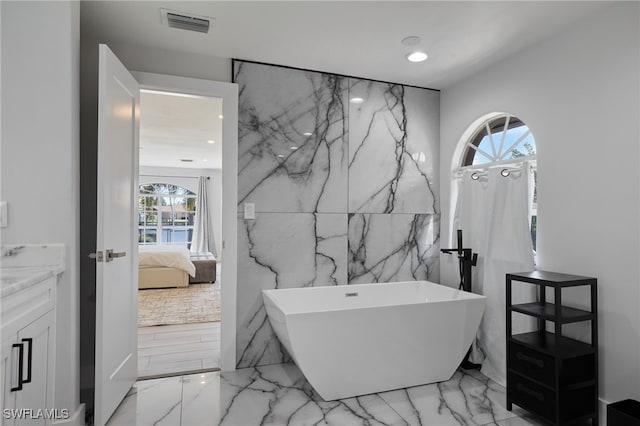 bathroom with marble finish floor, vanity, ensuite bath, a freestanding tub, and stone wall