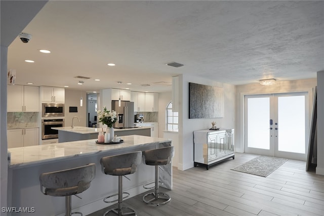 kitchen with tasteful backsplash, a center island with sink, stainless steel appliances, french doors, and white cabinetry