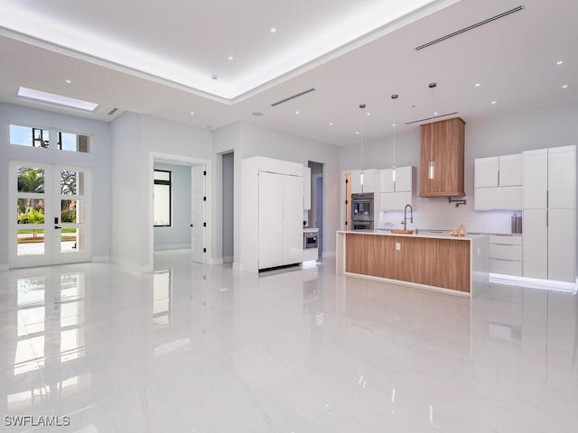 kitchen featuring white cabinets, modern cabinets, light countertops, a large island with sink, and pendant lighting