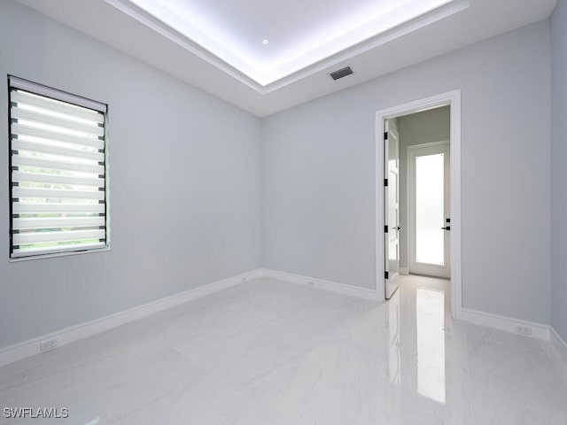 unfurnished room with marble finish floor, a tray ceiling, visible vents, and baseboards