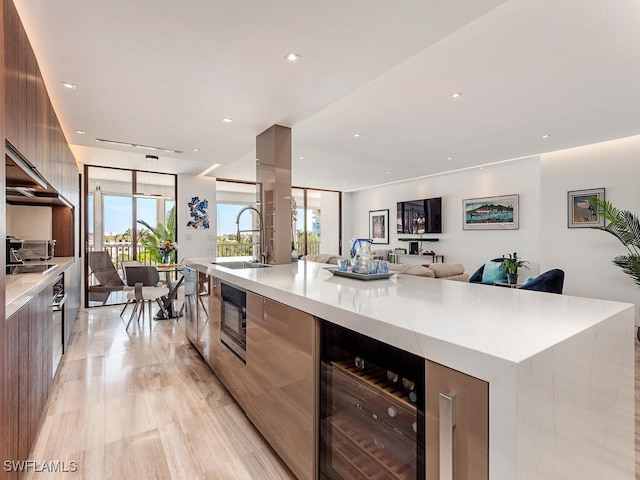 kitchen featuring a large island with sink, a sink, wine cooler, black microwave, and modern cabinets