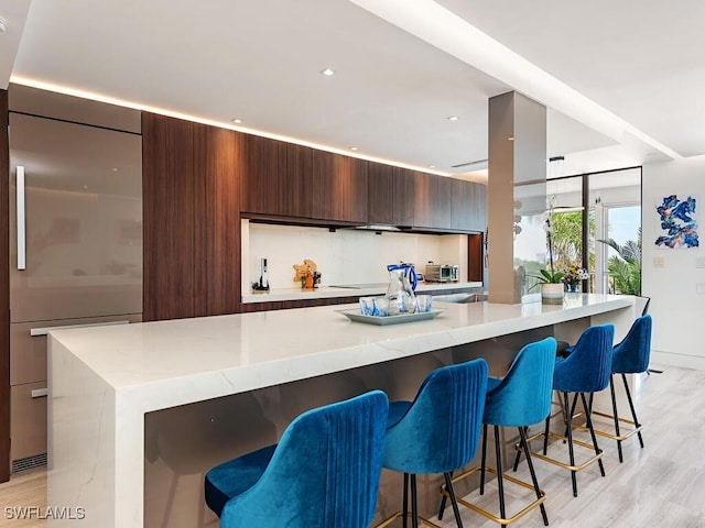 kitchen with a breakfast bar area, modern cabinets, light wood-style floors, and built in fridge