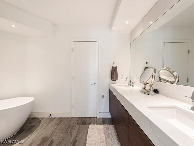 full bathroom with double vanity, a freestanding tub, wood finished floors, and a sink