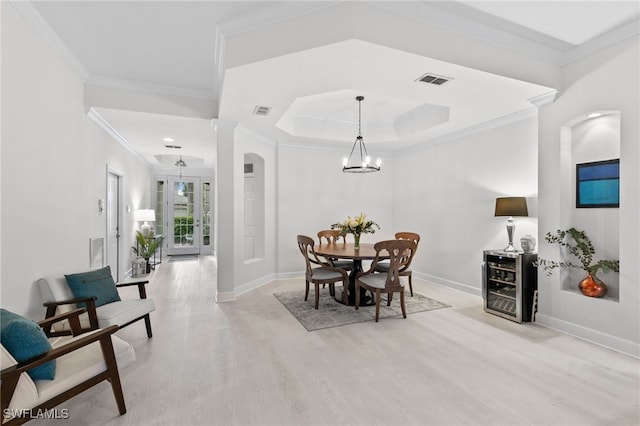 dining room with crown molding, an inviting chandelier, light wood-type flooring, and a tray ceiling