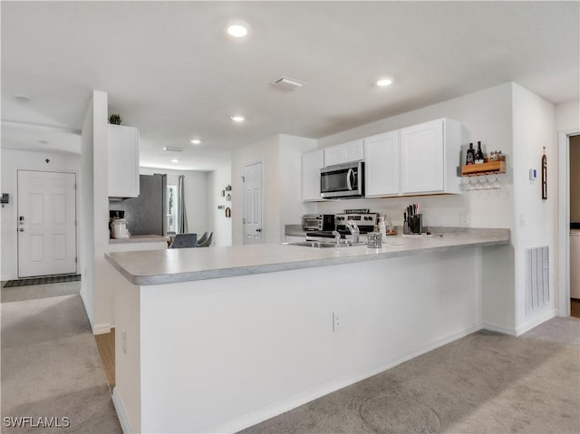 kitchen with appliances with stainless steel finishes, visible vents, a peninsula, and white cabinetry