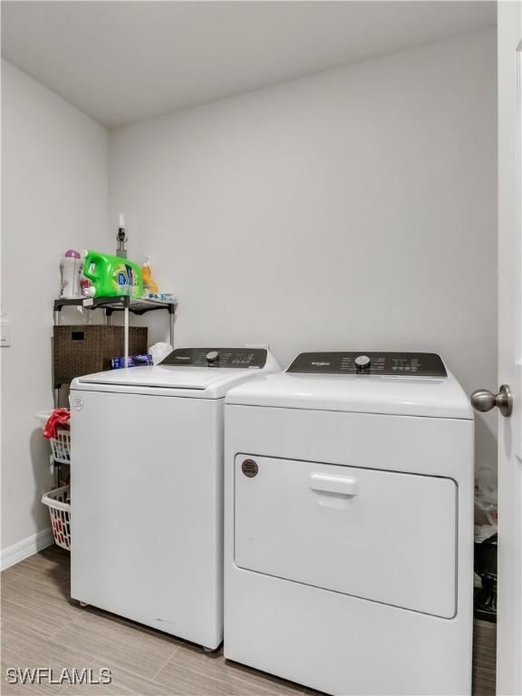 washroom featuring laundry area, baseboards, light wood-style flooring, and washing machine and clothes dryer