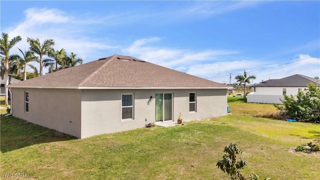 back of house with a shingled roof, a yard, and stucco siding