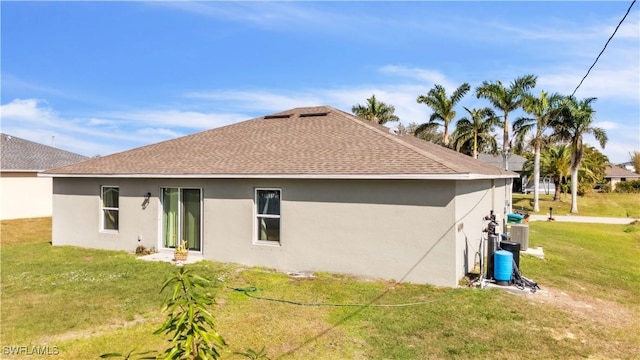 rear view of property with a shingled roof, stucco siding, a lawn, and central air condition unit