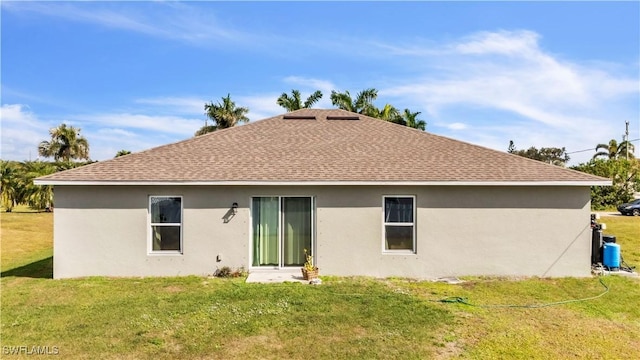 back of property with stucco siding, roof with shingles, and a yard