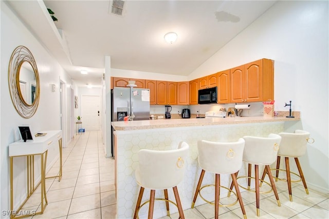 kitchen featuring light tile patterned floors, vaulted ceiling, kitchen peninsula, and a kitchen bar